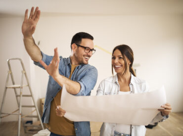 Young couple standing in their apartment while woman holding blueprint and man showing to her new ideas.